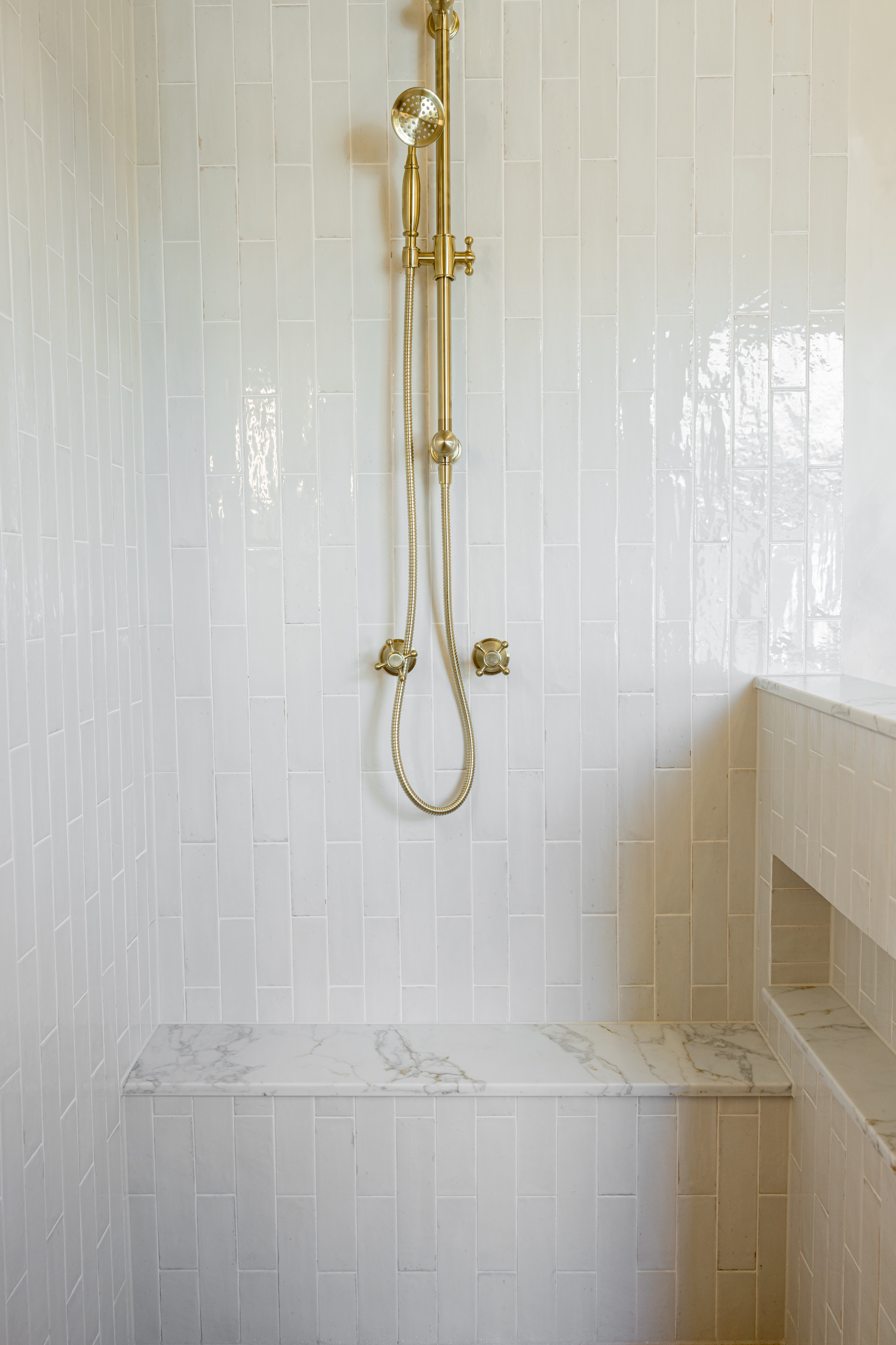 Shower with brass fixtures, marble bench seat and vertical tile pattern